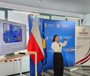 Hana Qerimi speaks at the meeting, beside the USAID banner